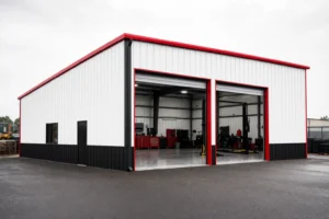 A tall mechanic shop metal building with open bay doors showing a two-post lift inside