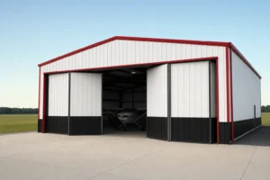 White metal airplane hangar with red trim and a wide bifold door partially open over a concrete apron