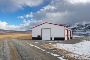 White steel building with red trim on an open rural site with sunny plains on one side and snowy foothills on the other