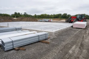 Metal building job site with a bare concrete slab, staged steel bundles, and a telehandler before erection begins