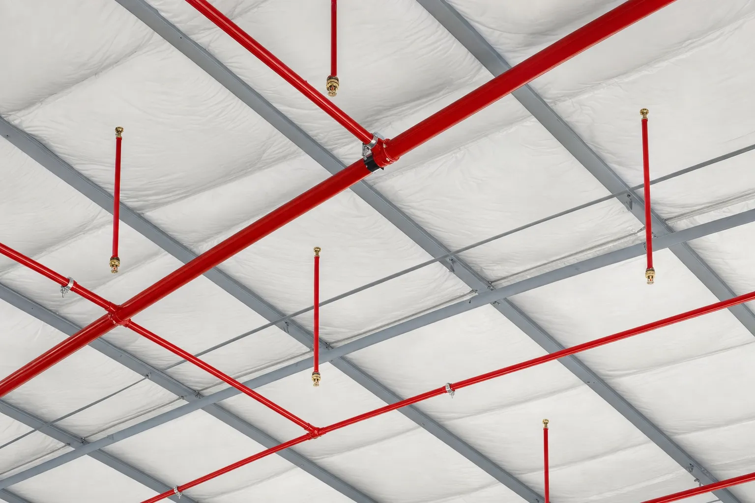 Red fire sprinkler piping and heads beneath the roof of a commercial metal building