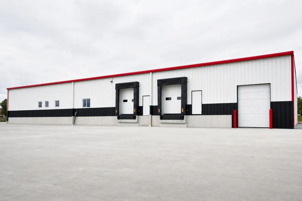 Metal Warehouse Cost: Shell, Foundation, Erection, and Buildout 2 A long commercial metal warehouse shell with loading dock doors and a concrete truck apron